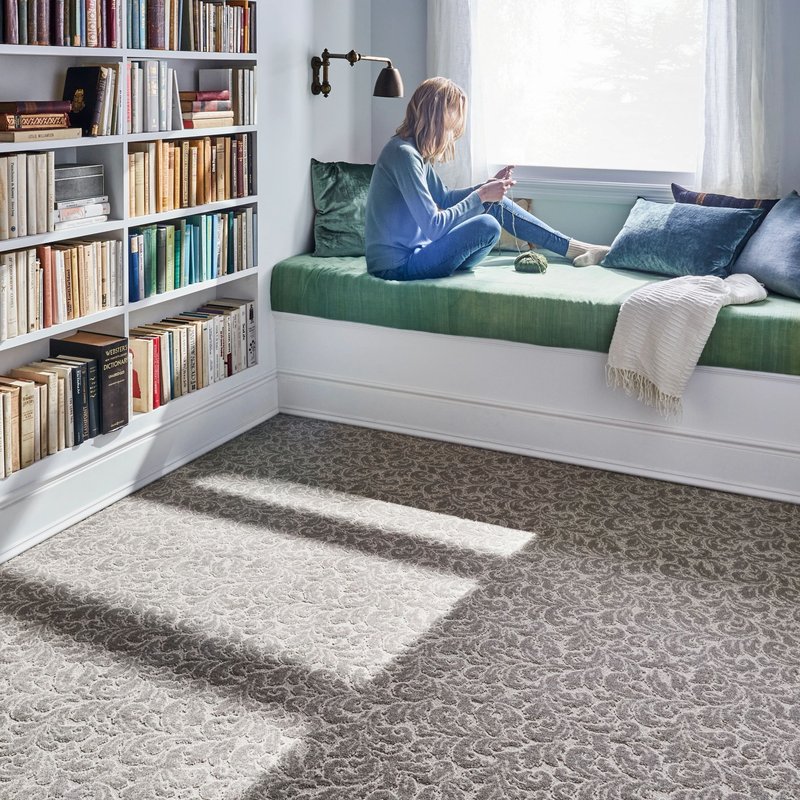 Woman looking through the window while knitting in a room with brown carpet floor from Direct Sales Floors in Danville, CA